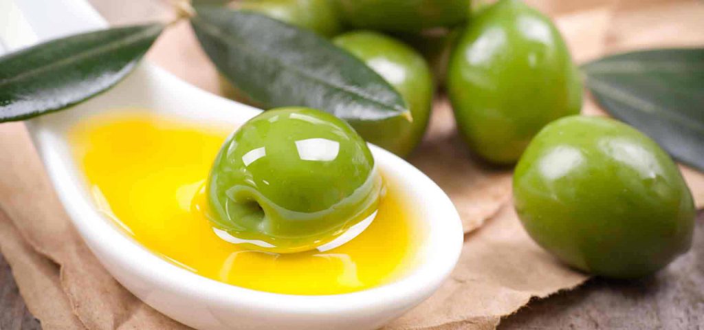 Olio extravergine di oliva italiano, oliva verde immersa nell'olio contenuto in un cucchiaio bianco di ceramica